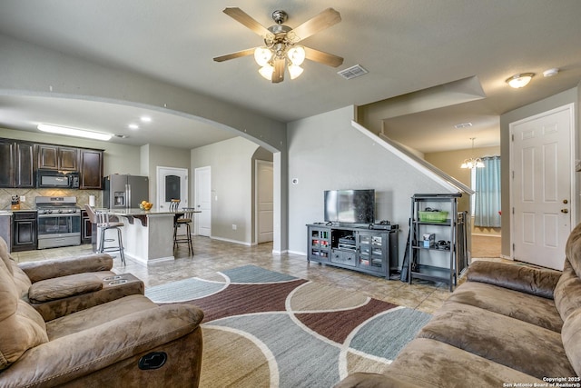 tiled living room with ceiling fan with notable chandelier