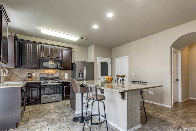 kitchen featuring a breakfast bar area, tasteful backsplash, a center island, stainless steel appliances, and light stone countertops