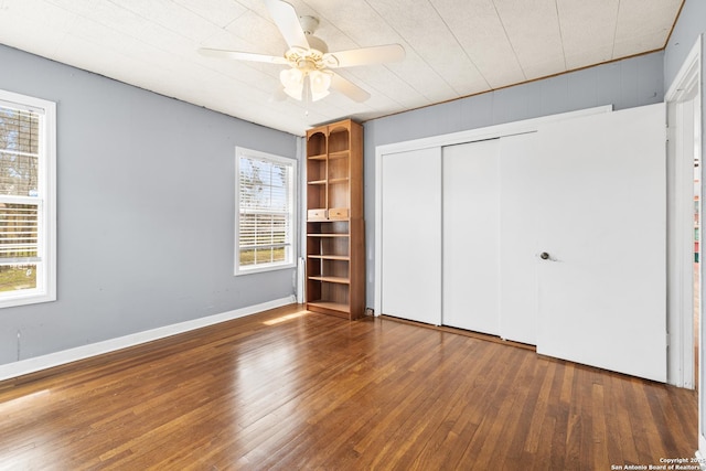 unfurnished bedroom with a closet, wood-type flooring, a ceiling fan, and baseboards