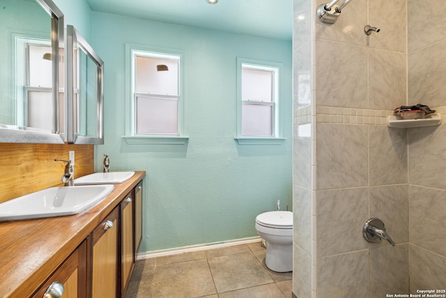 bathroom with double vanity, tiled shower, toilet, tile patterned flooring, and a sink