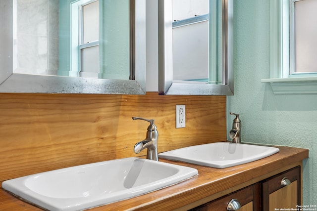 bathroom featuring a textured wall, double vanity, and a sink