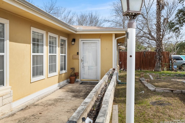 view of exterior entry featuring fence and stucco siding