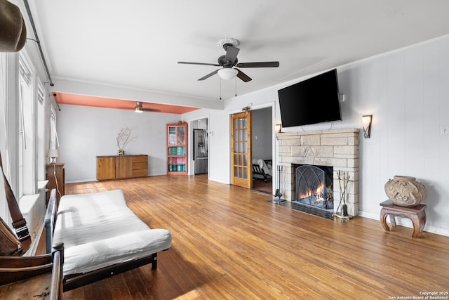 living area with ceiling fan, a fireplace, baseboards, and wood finished floors