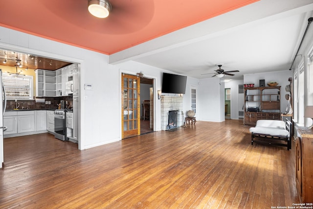 unfurnished living room with beam ceiling, a fireplace, a ceiling fan, a sink, and hardwood / wood-style floors