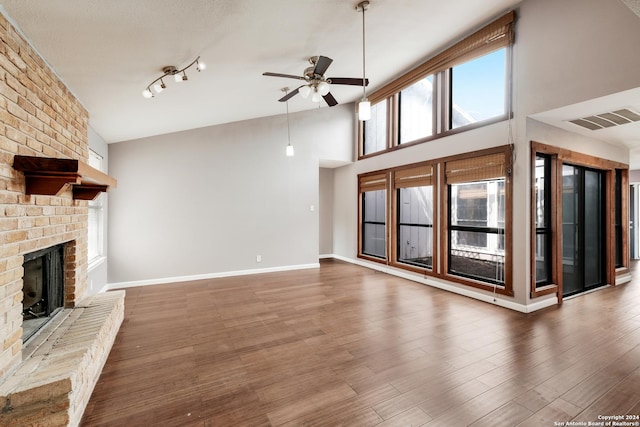 unfurnished living room with ceiling fan, a fireplace, hardwood / wood-style floors, and a towering ceiling