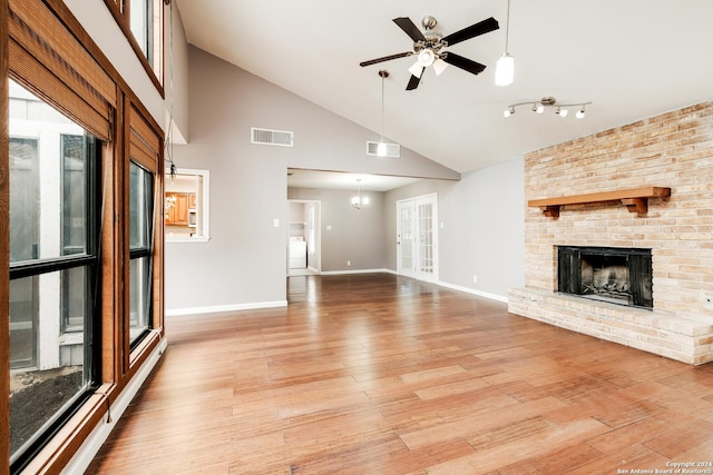 unfurnished living room featuring plenty of natural light, ceiling fan with notable chandelier, a brick fireplace, and light hardwood / wood-style flooring