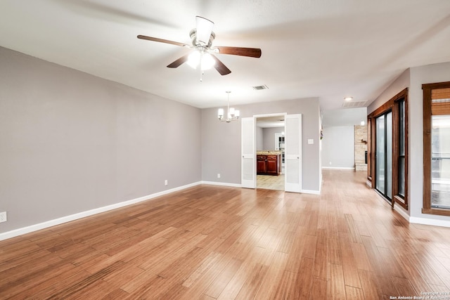 unfurnished living room with ceiling fan with notable chandelier and light hardwood / wood-style flooring