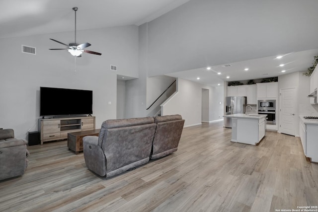 living room with sink, light hardwood / wood-style flooring, high vaulted ceiling, and ceiling fan