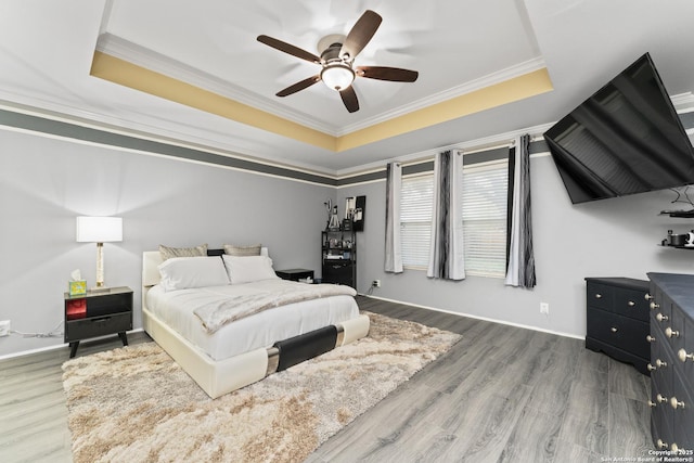 bedroom featuring a tray ceiling, wood-type flooring, ornamental molding, and ceiling fan