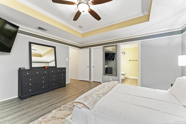 bedroom with hardwood / wood-style flooring, ensuite bath, ceiling fan, ornamental molding, and a raised ceiling