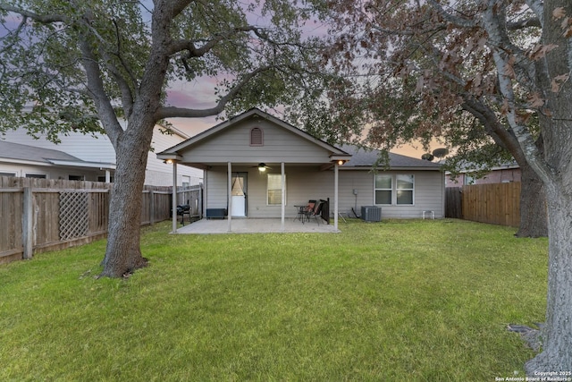 back house at dusk featuring a patio, central AC, ceiling fan, and a lawn