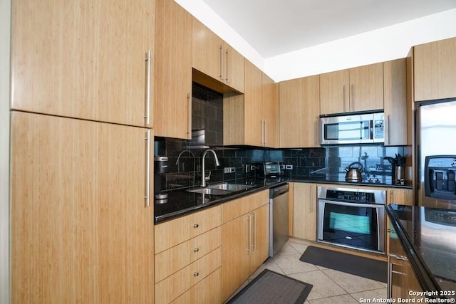 kitchen with sink, light tile patterned floors, appliances with stainless steel finishes, backsplash, and dark stone counters