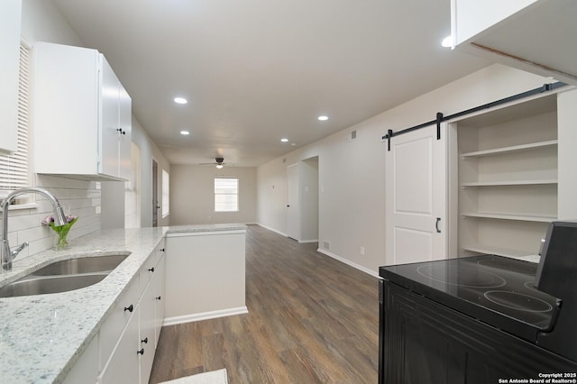 kitchen with sink, white cabinetry, light stone counters, kitchen peninsula, and a barn door