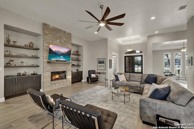 living room with built in features, ceiling fan, light hardwood / wood-style floors, a textured ceiling, and a stone fireplace