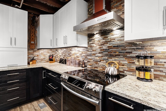 kitchen with white cabinetry, wall chimney range hood, light stone counters, and electric stove