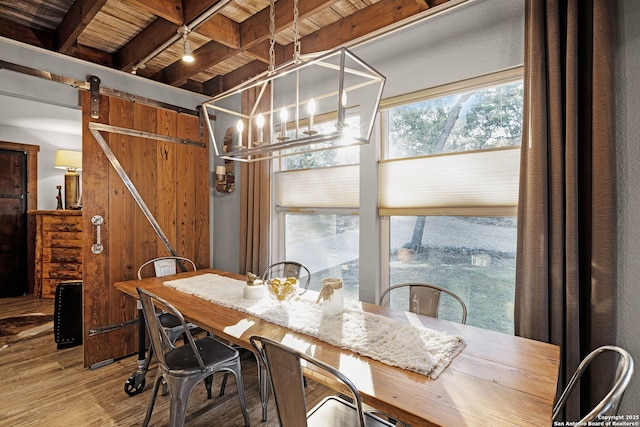 dining space featuring a barn door, hardwood / wood-style floors, and beam ceiling