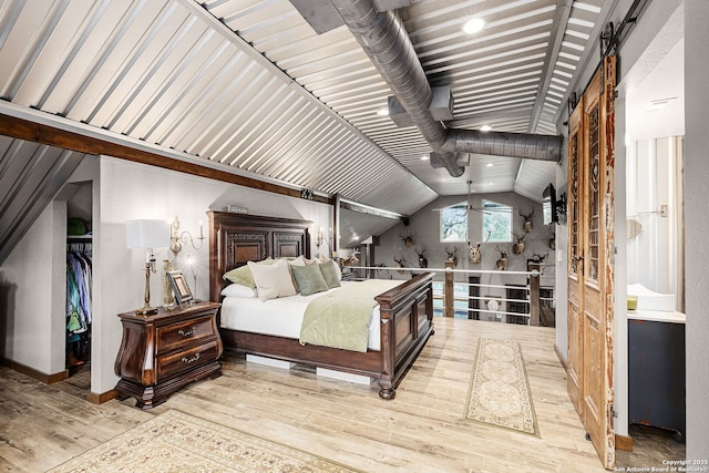 bedroom with a barn door, lofted ceiling, a spacious closet, and light hardwood / wood-style floors