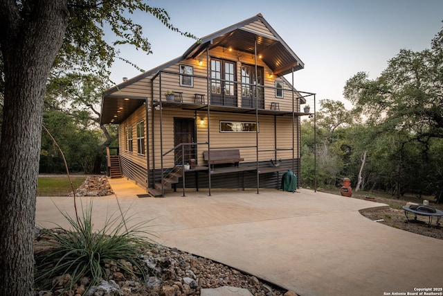 back house at dusk featuring a balcony and an outdoor fire pit