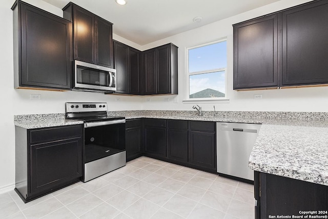 kitchen with appliances with stainless steel finishes, light stone countertops, sink, and light tile patterned floors