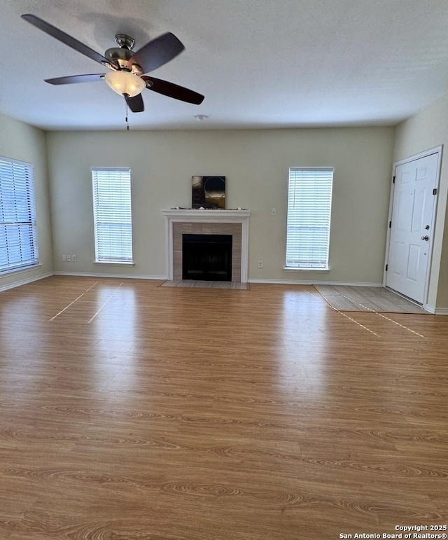 unfurnished living room with hardwood / wood-style flooring, plenty of natural light, a tile fireplace, and ceiling fan