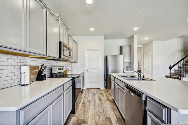 kitchen with sink, light wood-type flooring, gray cabinets, an island with sink, and stainless steel appliances