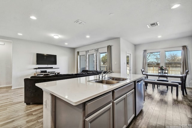 kitchen featuring sink, light hardwood / wood-style flooring, plenty of natural light, dishwasher, and an island with sink