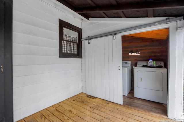 laundry area with light hardwood / wood-style flooring, washing machine and dryer, a barn door, and wood walls