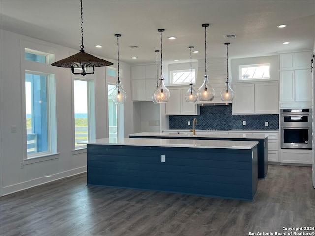 kitchen featuring a center island with sink, pendant lighting, white cabinets, and double oven