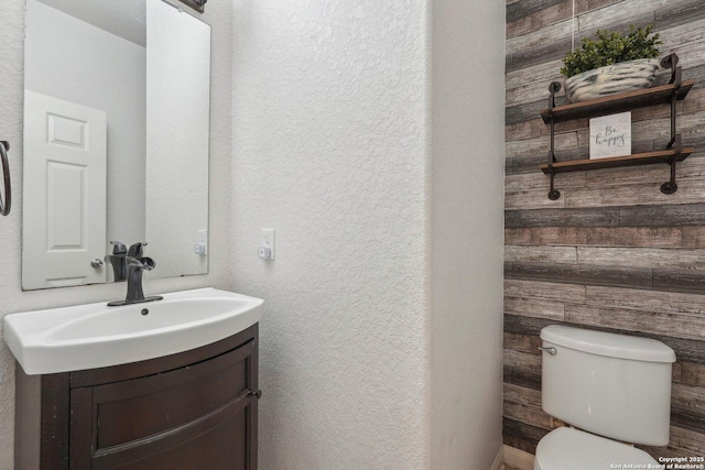 bathroom featuring vanity, toilet, and wood walls