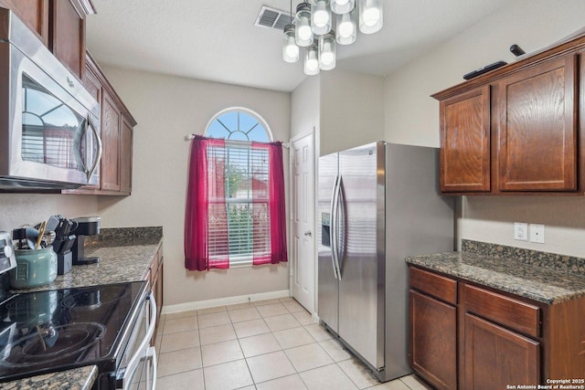 kitchen with stainless steel appliances, dark stone countertops, an inviting chandelier, and light tile patterned floors