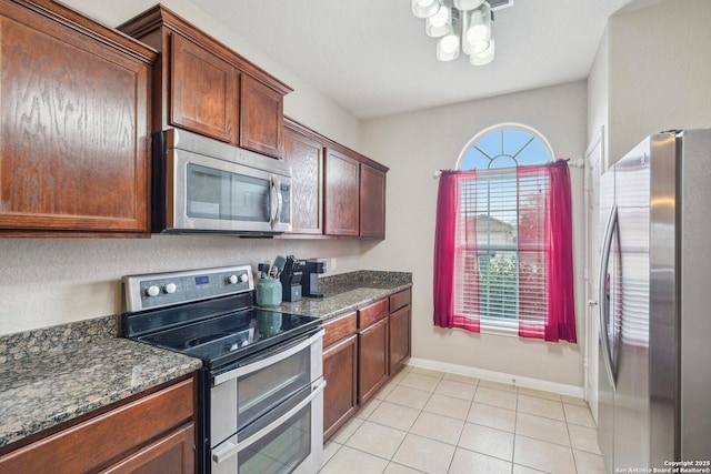 kitchen with light tile patterned flooring, dark stone counters, and appliances with stainless steel finishes