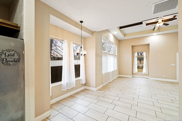 interior space with a tray ceiling, ceiling fan with notable chandelier, and light tile patterned floors