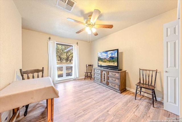 living area featuring a textured ceiling, light hardwood / wood-style floors, and ceiling fan