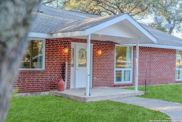 view of exterior entry featuring a patio and a lawn