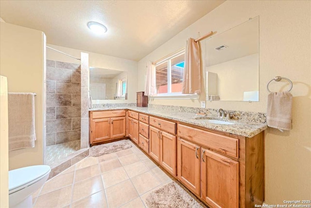 bathroom featuring vanity, tile patterned flooring, toilet, and tiled shower