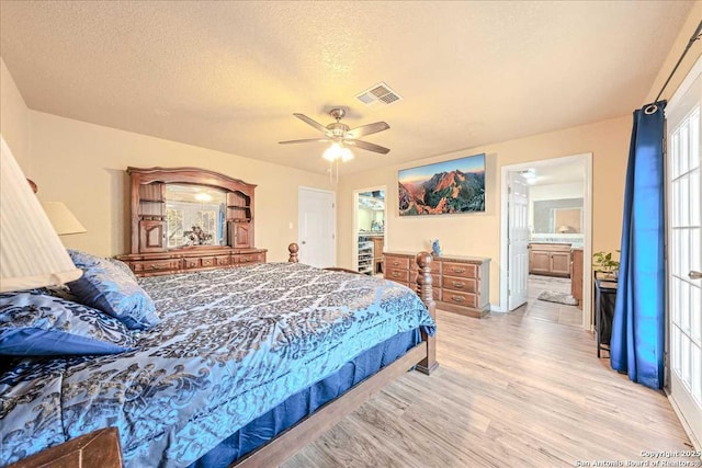 bedroom with ceiling fan, ensuite bath, light hardwood / wood-style floors, and a textured ceiling