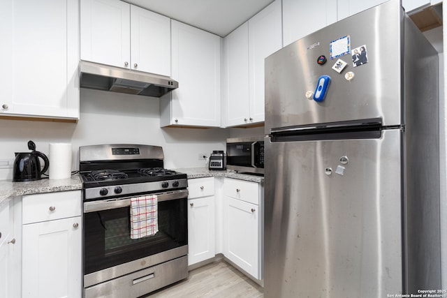 kitchen with light stone countertops, appliances with stainless steel finishes, white cabinets, and light hardwood / wood-style floors