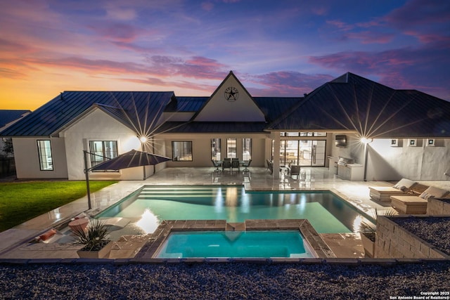 pool at dusk with an in ground hot tub, an outdoor kitchen, and a patio area