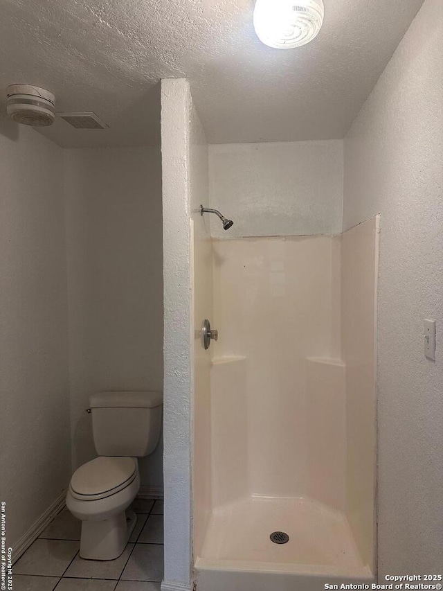 bathroom featuring tile patterned flooring, a textured ceiling, toilet, and a shower