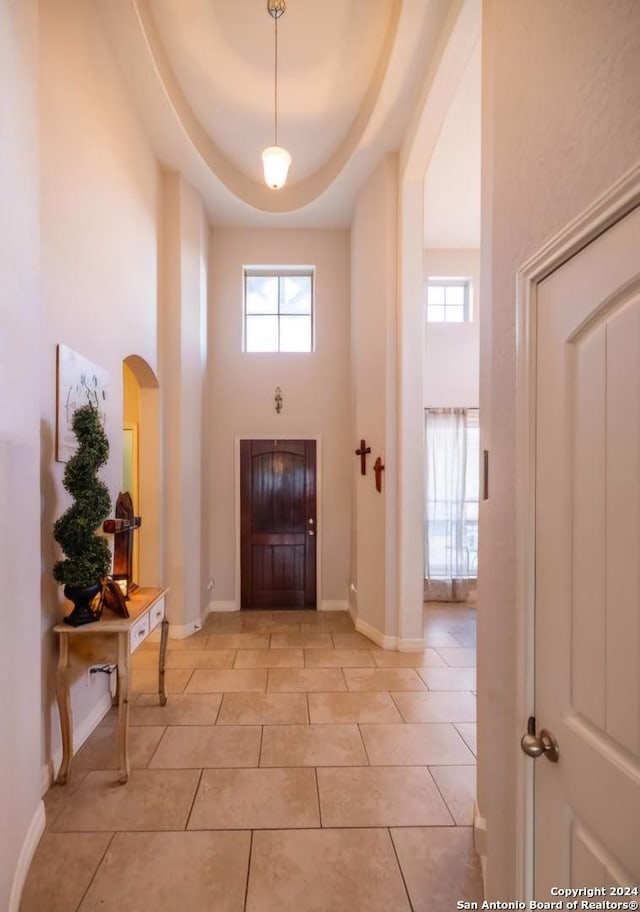 foyer entrance with light tile patterned flooring, a towering ceiling, a tray ceiling, and a wealth of natural light