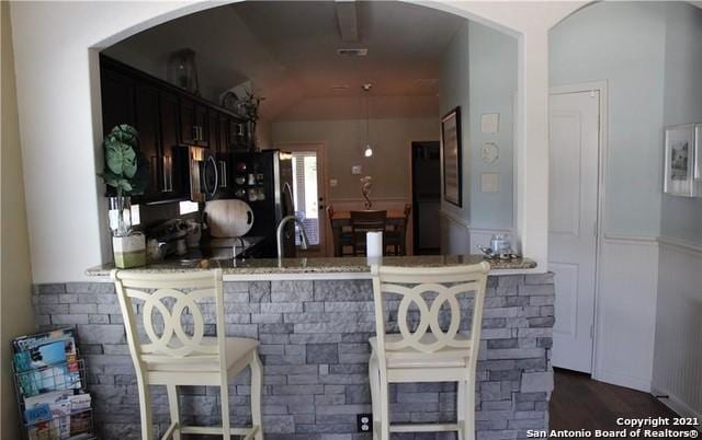 kitchen featuring stove, black fridge, kitchen peninsula, light stone countertops, and dark brown cabinets