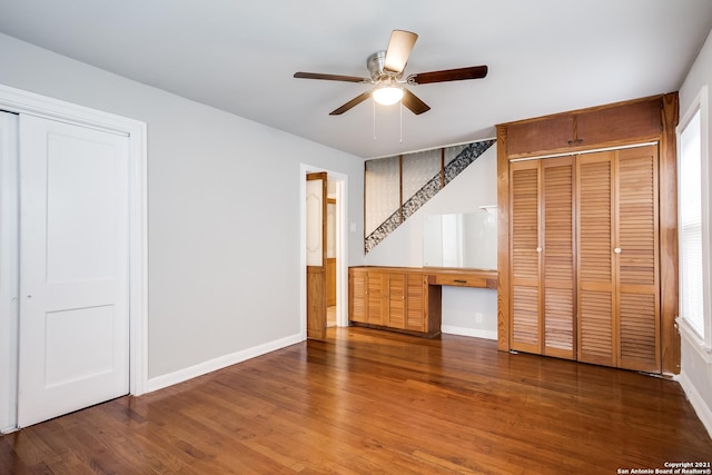 unfurnished bedroom featuring hardwood / wood-style floors, built in desk, multiple closets, and ceiling fan