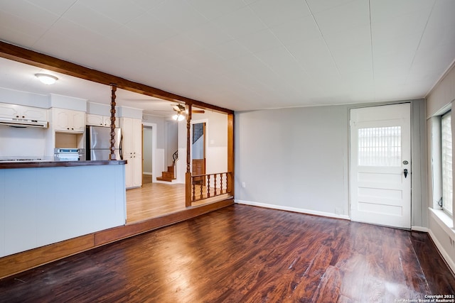 unfurnished living room featuring beam ceiling, dark hardwood / wood-style floors, and ceiling fan