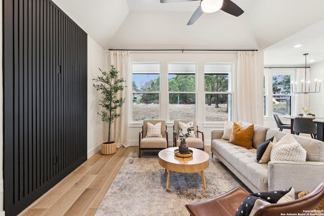 living room featuring vaulted ceiling, ceiling fan with notable chandelier, and light wood-type flooring