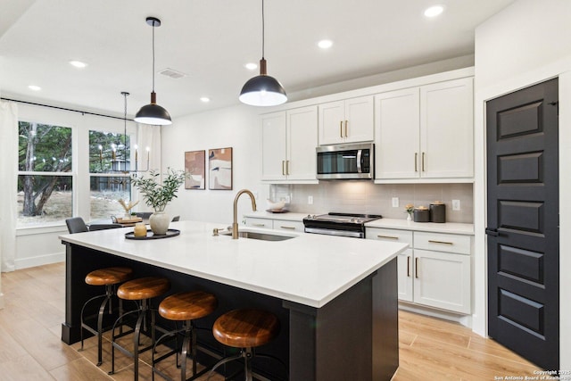 kitchen featuring an island with sink, appliances with stainless steel finishes, sink, and white cabinets