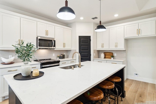 kitchen featuring stainless steel appliances, an island with sink, sink, and decorative light fixtures