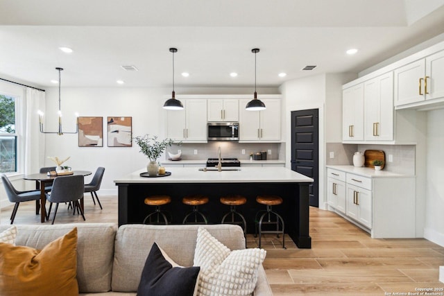 kitchen featuring hanging light fixtures, an island with sink, and white cabinets