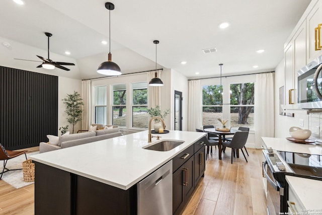 kitchen with sink, appliances with stainless steel finishes, a kitchen island with sink, hanging light fixtures, and white cabinets