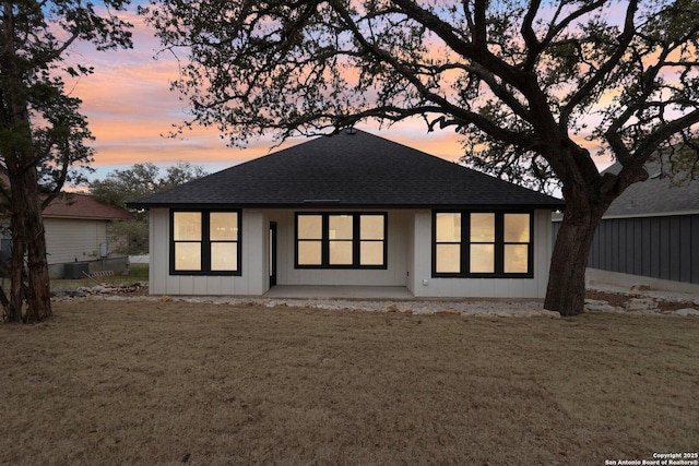 back house at dusk featuring a lawn