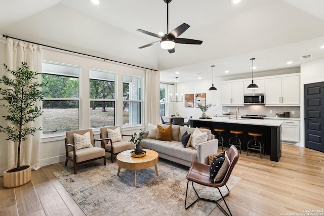 living room featuring ceiling fan, lofted ceiling, sink, and light wood-type flooring